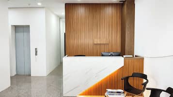 Zona de recepción con mostrador de mármol, panel de pared de madera y sillas negras.