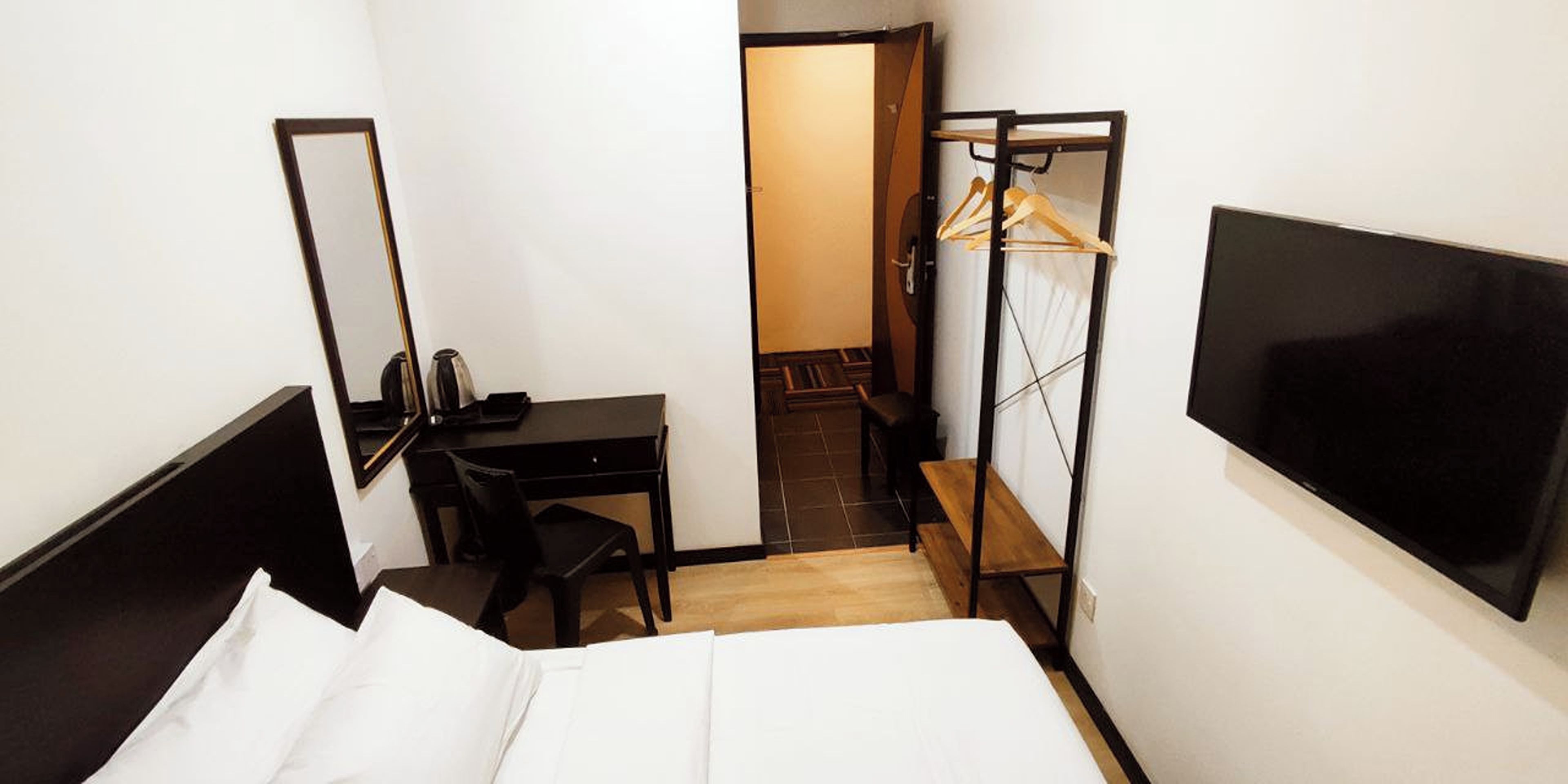 Ein Hotelzimmer mit einem Bett, einem Schreibtisch, einem Stuhl, einem Fernseher und einem Kleiderschrank mit Spiegel.