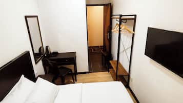 Ein Hotelzimmer mit einem Bett, einem Schreibtisch, einem Stuhl, einem Fernseher und einem Kleiderschrank mit Spiegel.
