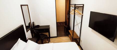 Ein Hotelzimmer mit einem Bett, einem Schreibtisch, einem Stuhl, einem Fernseher und einem Kleiderschrank mit Spiegel.