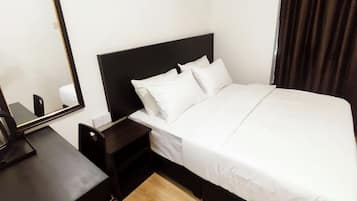 A hotel room with a bed, a bedside table with a kettle, a small drawer, and a mirror on the wall.