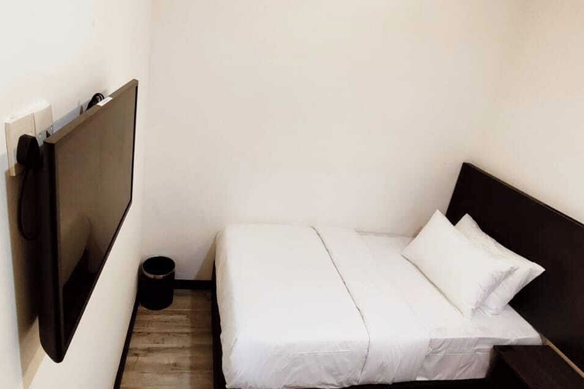 Et lille, smalt hotelværelse med en enkelt seng, trægulv og en sort skraldespand.