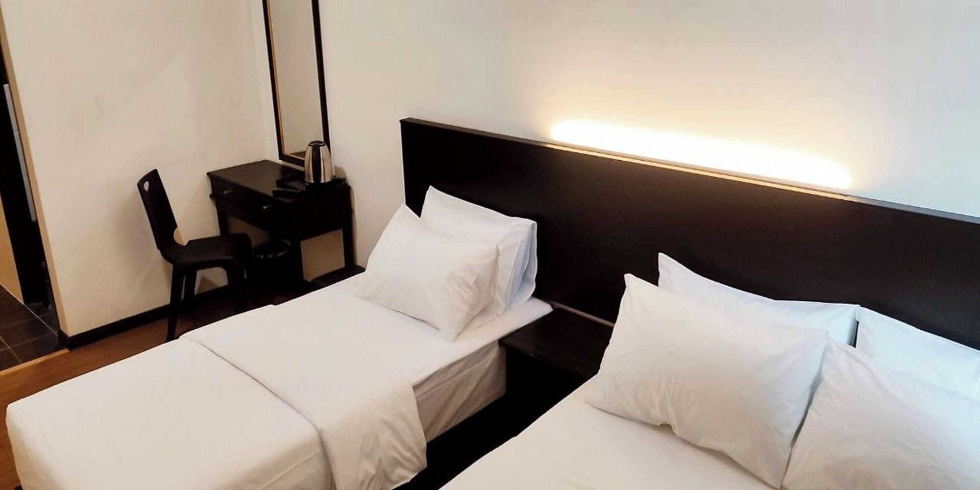 Una camera d'albergo con due letti singoli, una scrivania con sedia e un comodino con lampada.