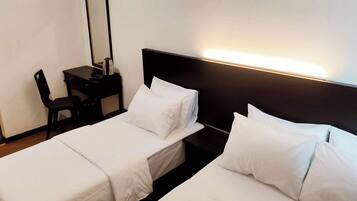 A hotel room with two single beds, a desk with a chair, and a nightstand with a lamp.