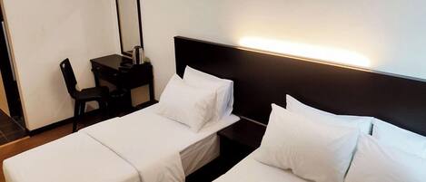 A hotel room with two single beds, a desk with a chair, and a nightstand with a lamp.