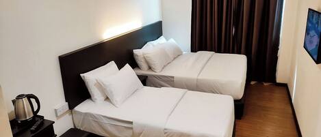 A hotel room with two single beds, a nightstand with a kettle, and a TV mounted on the wall.
