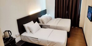 Una habitación de hotel con dos camas individuales, una mesita de noche con hervidor y un televisor montado en la pared.