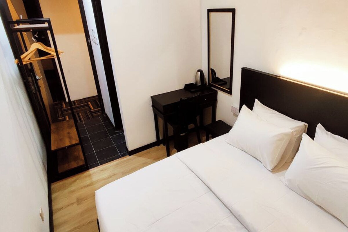 Habitación de hotel con una cama grande, una mesita de noche, un espejo y suelo de madera.