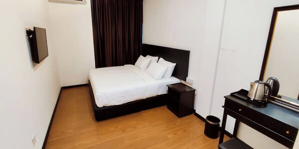 A hotel room with a bed, a nightstand, a small table with a kettle, and a trash can.