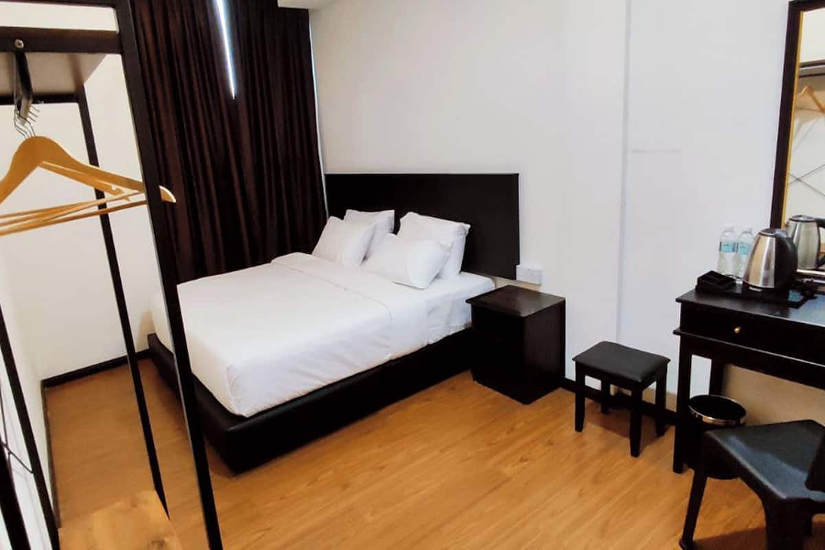 Quarto de hotel com cama, escrivaninha, cadeira, cabideiro e espelho.