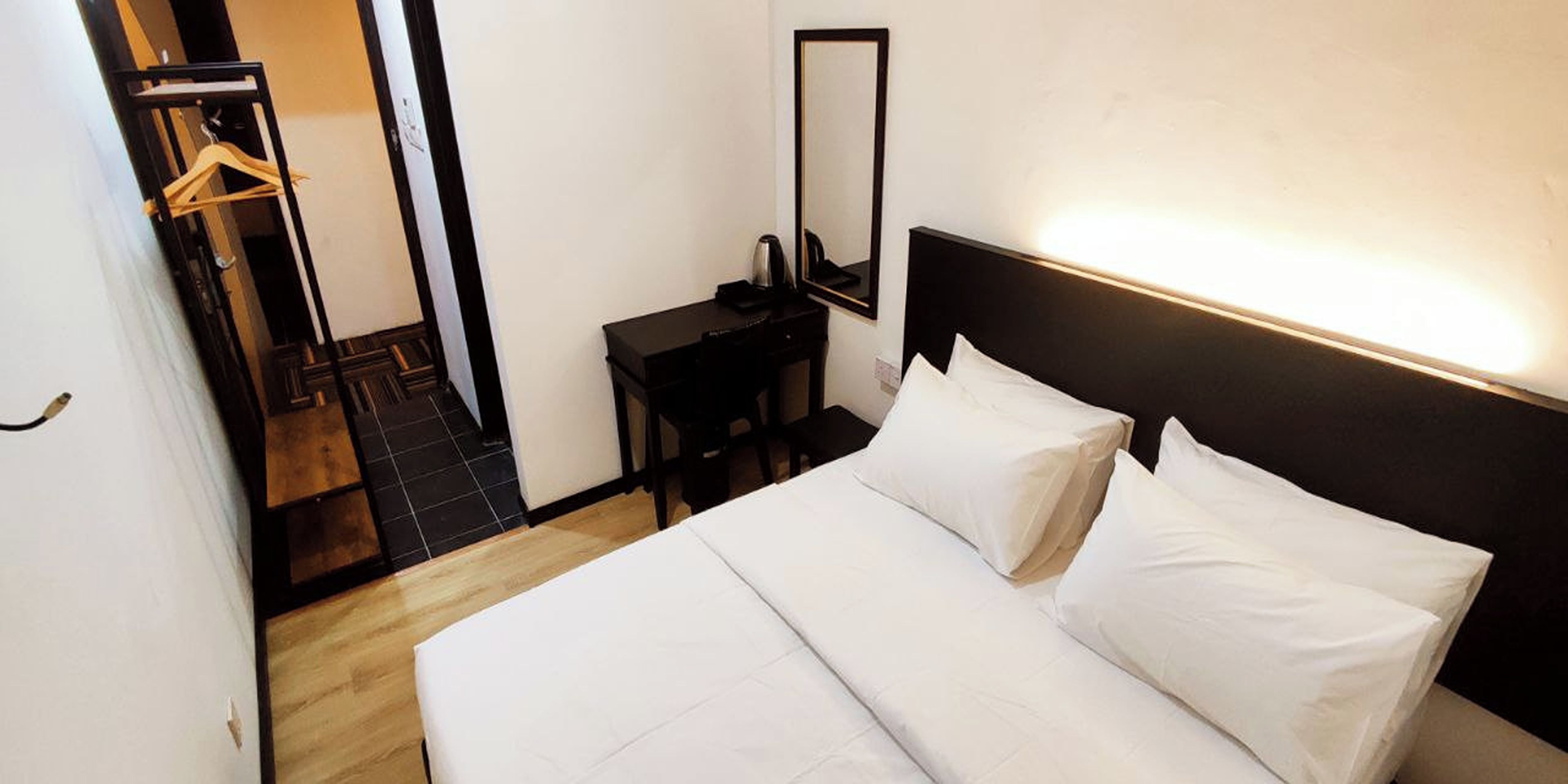 Quarto de hotel com uma cama grande, mesa de cabeceira, espelho e piso de madeira.