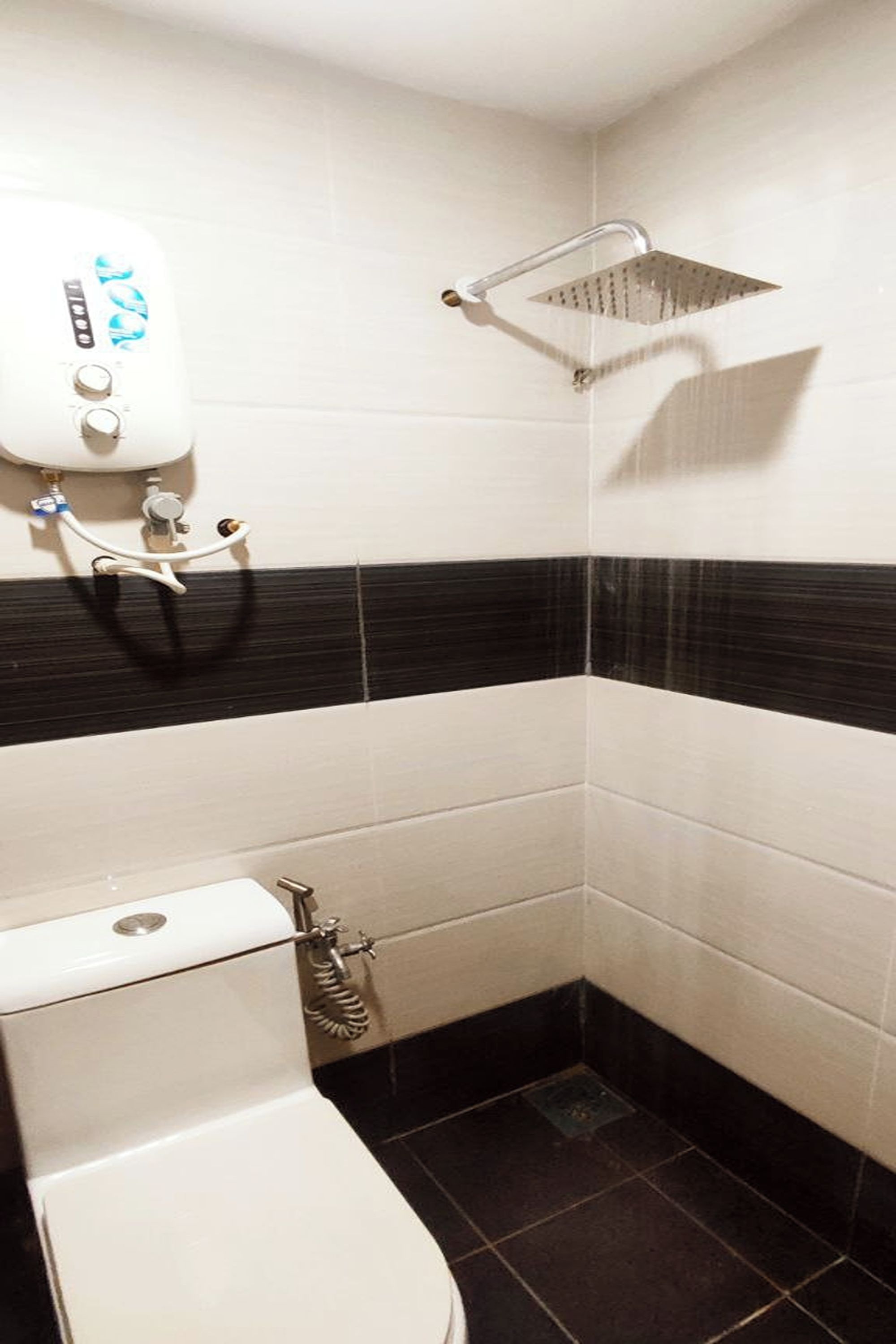 Ein Badezimmer im Eckbereich mit Toilette, Dusche und Durchlauferhitzer.