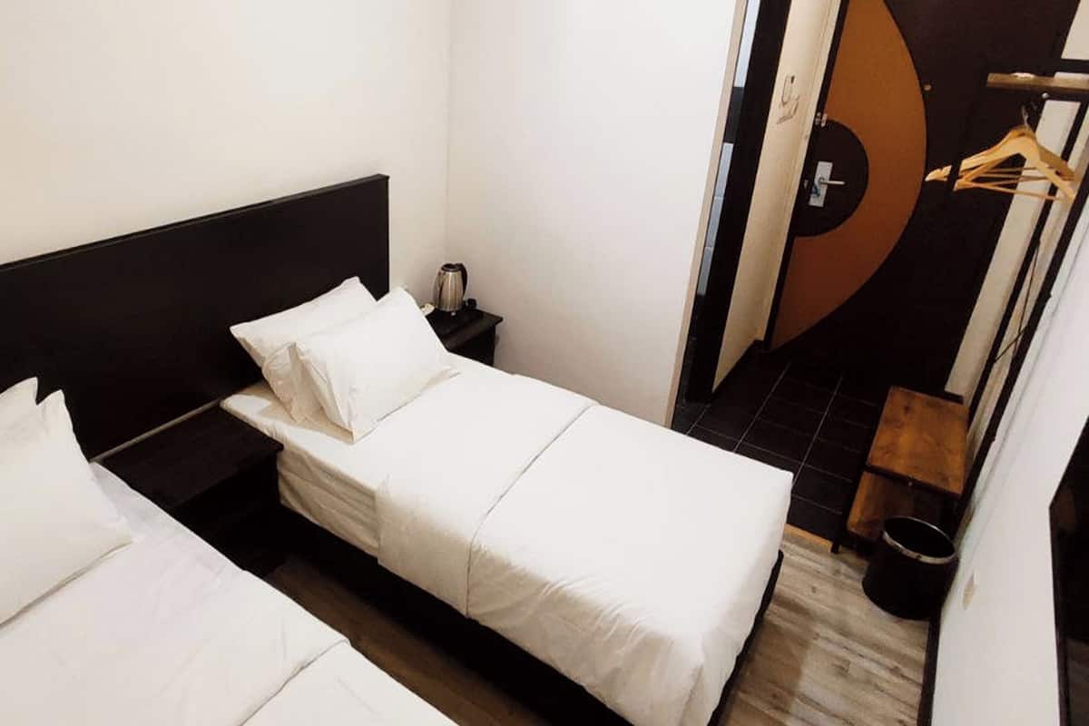 Quarto de hotel com duas camas de solteiro, uma pequena mesa de cabeceira, um cabideiro e vista para o interior.