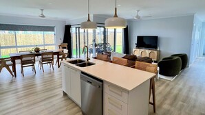 Una cocina amplia con una isla central, un comedor con mobiliario de madera y una sala de estar con televisor y asientos.