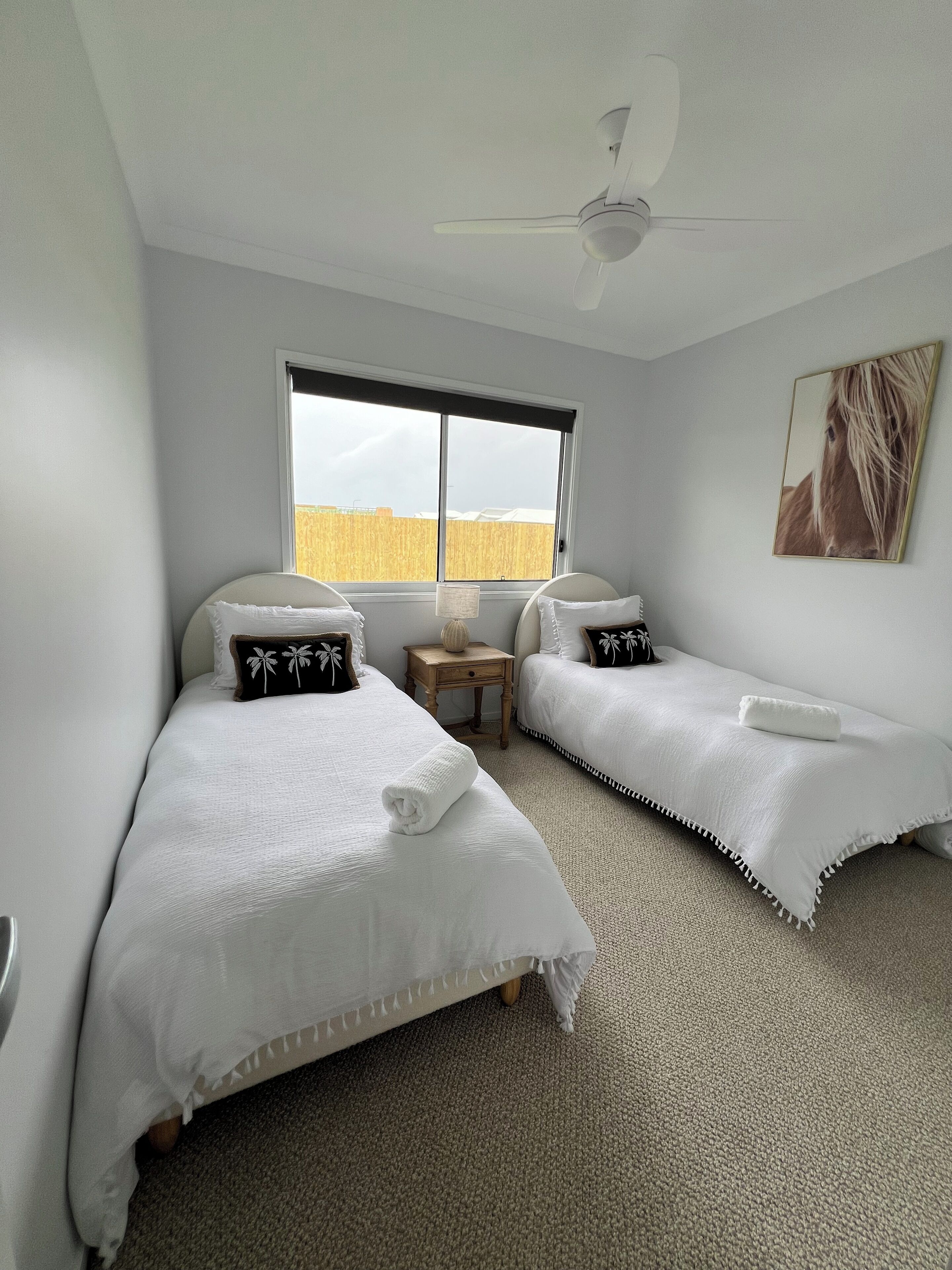 Una camera da letto con due letti singoli, una ventola a soffitto, una finestra vista campo e un quadro appeso al muro.