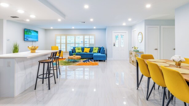 A modern living room with a blue sofa, yellow chairs, and a dining area with yellow chairs. - Private Pool, Patio & BBQ Near Beaches & Casino (Margate)
