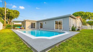 A modern house with a swimming pool, a covered patio, and a well-maintained lawn.