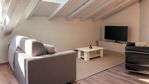 A modern loft-style living room with a sloped ceiling, a sofa, a coffee table, and a TV. - [SKY Cinema] Elegance and design in the heart of Trento (Trento)