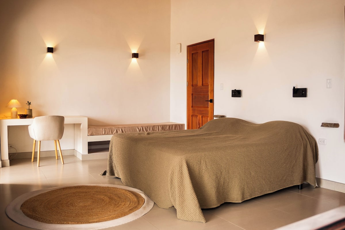 A bedroom with a bed, bedside table, lamp, chair, and wall-mounted light fixtures.
