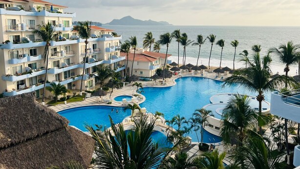 Un resort con una piscina grande, varios balcones y vista al océano.
