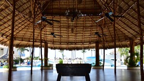 Un espacio al aire libre techado con un banco, ventiladores de techo y una piscina al fondo.