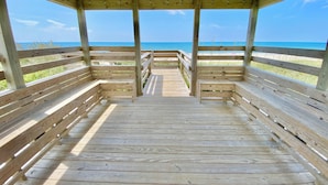 Une terrasse en bois qui mène à une plage et offre une vue dégagée sur l’océan.
