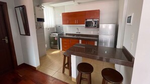 A compact kitchen with a central island, wooden cabinets, a microwave, and a refrigerator. - Skyline Suites (La Paz)