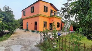 Une maison à deux étages, avec une façade rouge et jaune, un escalier apparent et un jardin qui l’entoure.