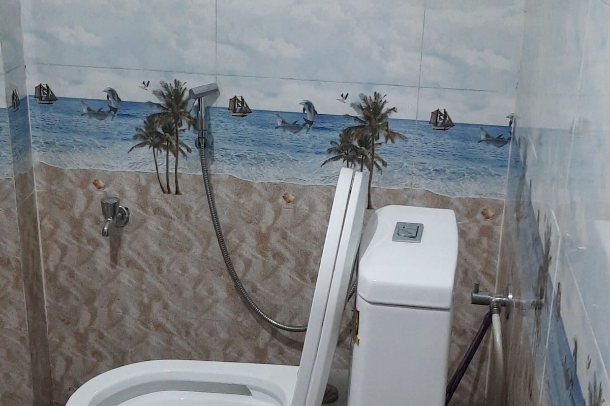 Un baño con inodoro, ducha y pared de azulejos que representa una escena de playa.