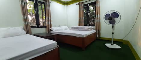 A room with two beds, a standing fan, and a window with curtains.