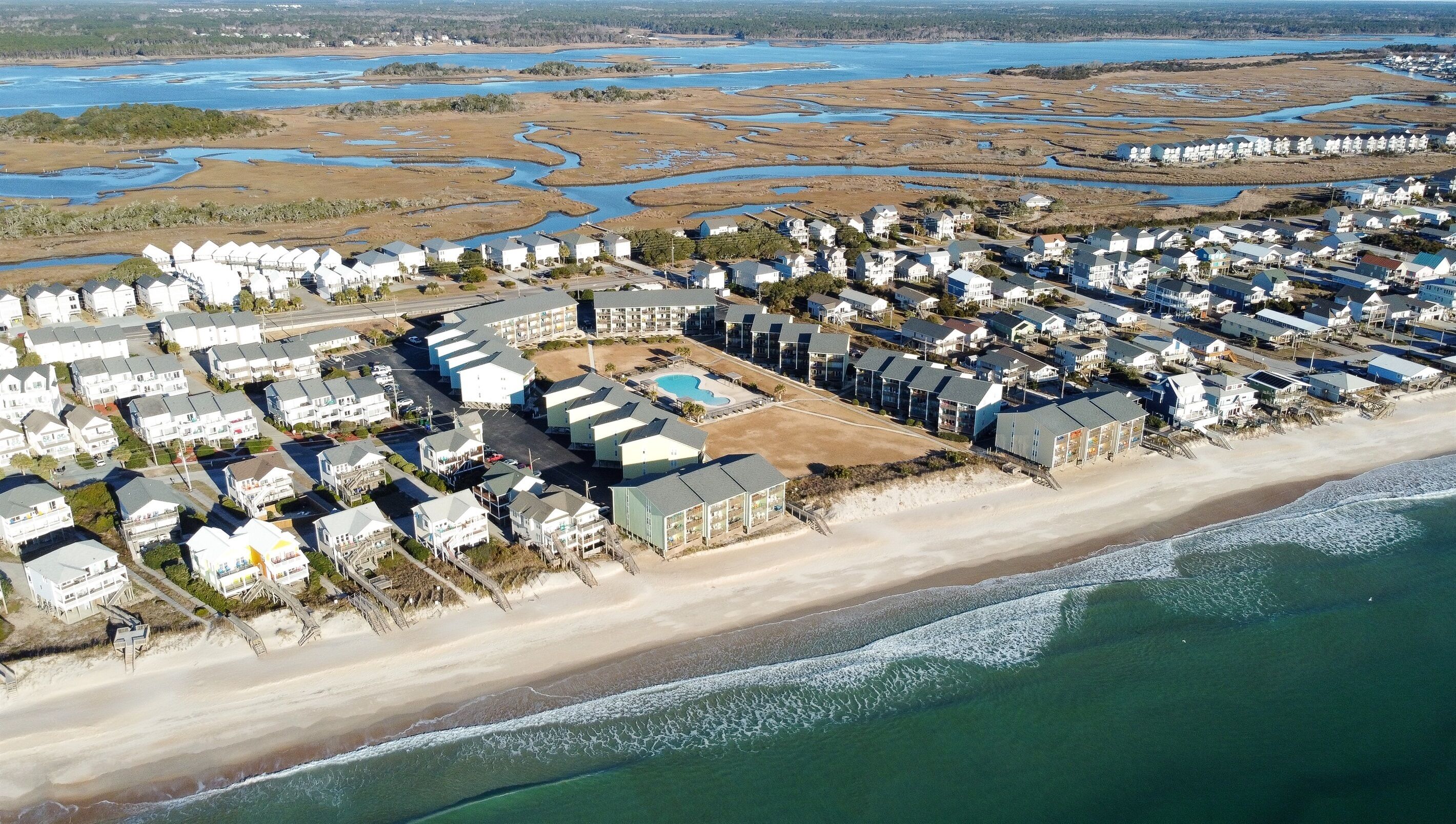 Ett flygbildsfoto av ett bostadsområde vid kusten med hus, en strand och en stor vattenyta.