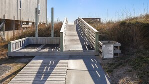 En træpromenade der fører hen til en strand med et skilt.