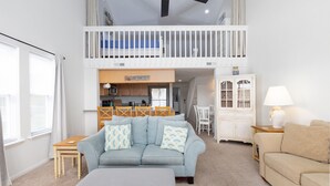 En rummelig opholdsstue med højt til loftet, et spisebord, en sofa og et køkkenhjørne.