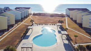 Et resort med en central pool, udsigt til stranden og flere bygninger.