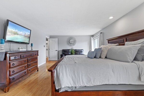 A bedroom with a large bed, wooden dresser, and a television on the wall. - Spacious 5-bedroom house in charming New London, CT with WiFi & a Game Room. (New London)