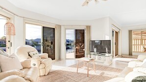 A spacious living room with a large TV, comfortable seating, and a view of a pool and outdoor area. - The Stately Way, Wallaroo (Wallaroo)