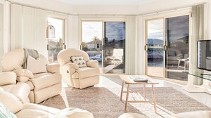 A spacious living room with a beige sofa set, a coffee table, and a television. Large glass doors lead to an outdoor patio area. - The Stately Way, Wallaroo (Wallaroo)