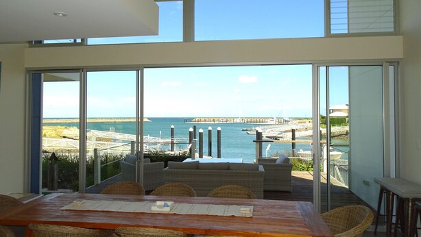Una habitación moderna con un gran ventanal que da a un balcón con vistas al mar y al muelle.