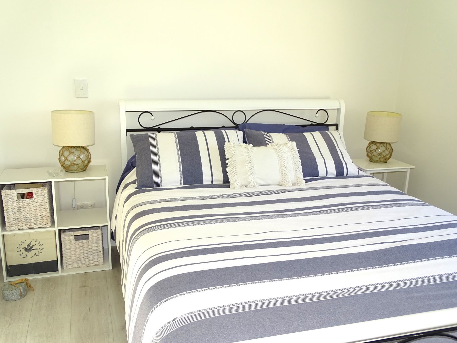 A neatly made bed with striped bedding, two bedside tables with lamps, and storage units under the bed.