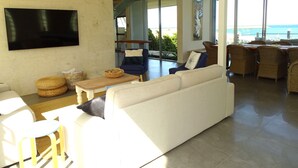 Un salón espacioso con un televisor de pantalla plana grande, asientos cómodos y vista al océano.