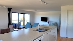 A modern kitchen with a dishwasher, a large window, and a dining area with blue chairs. - Sturt Bay Retreat, Port Moorowie (Warooka)
