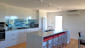 A modern kitchen with white cabinets, a large island with red bar stools, a microwave, and a gas stove. - Sturt Bay Retreat, Port Moorowie (Warooka)