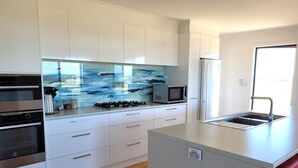 A modern kitchen with white cabinets, a stainless steel range, a microwave, and a large window with a view of the ocean. - Sturt Bay Retreat, Port Moorowie (Warooka)