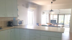 Una cucina moderna con mobili bianchi, un forno a microonde e una macchina da caffè. C'è una zona pranzo con tavolo e sedie, e un'ampia finestra che offre luce naturale.