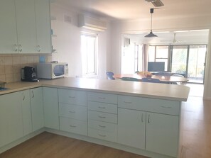 A modern kitchen with white cabinets, a microwave, and a coffee maker. There is a dining area with a table and chairs, and a large window providing natural light.
