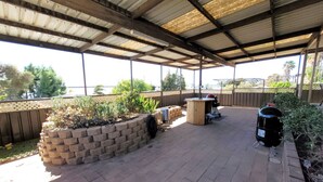 Una veranda esterna con pavimento in mattoni, una postazione barbecue in legno e una griglia.