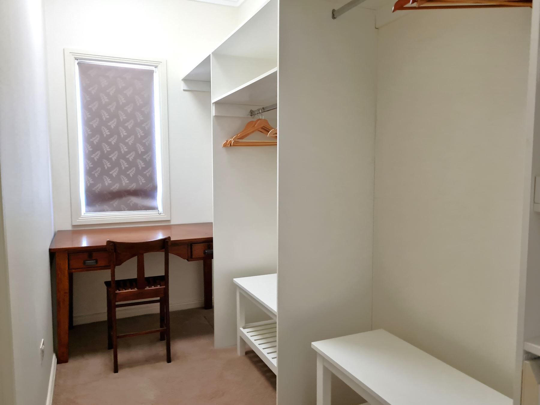 Ein kleiner, gut beleuchteter Raum mit Schreibtisch, Stuhl und einem begehbaren Kleiderschrank mit Kleiderstange.