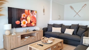 Ein modernes Wohnzimmer mit Flachbildfernseher, Holzmöbeln, einem grauen Sofa und dekorativen Kissen.