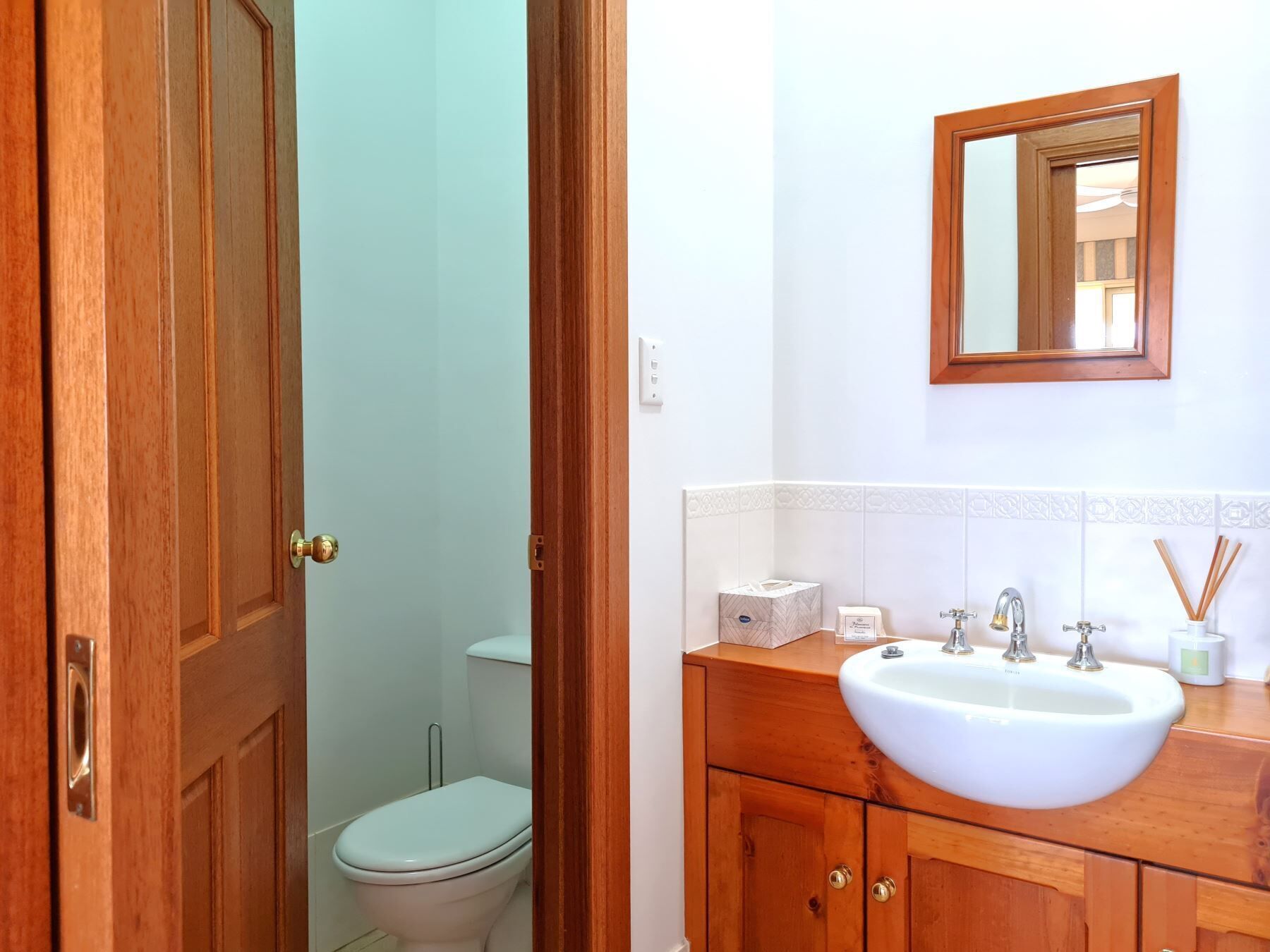 Ein Badezimmer mit einem Holzkosmetikschrank, einem weißen Waschbecken und einem Spiegel darüber.