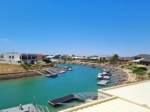 Un port de plaisance où sont amarrés des bateaux, entouré de maisons modernes dotées de panneaux solaires, et un ciel bleu dégagé.